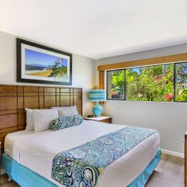 Bedroom at Gardens at West Maui with large bed, teal lamps, and garden window.